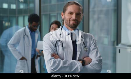 Portrait confident happy Caucasian man doctor smiling posing with crossed hands near medicine workers team colleagues in clinic. Cheerful professional Stock Photo