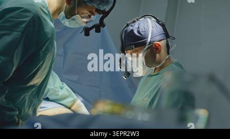 Close up two males surgeons in medical masks doctors men wearing advanced surgery loupes lights working operating in hospital clinic physicians Stock Photo