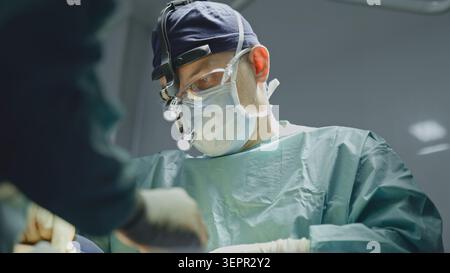 Two doctors surgeons in uniform mask physicians medics men operating communicating during operation. Caucasian man surgeon with medical nurse operate Stock Photo