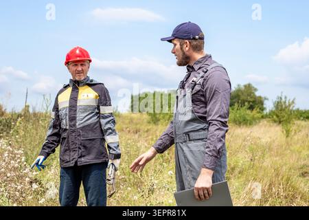 Two technical specialists discuss plans holding a tablet on a field site. engineering audit, industrial inspection, site planning. Stock Photo