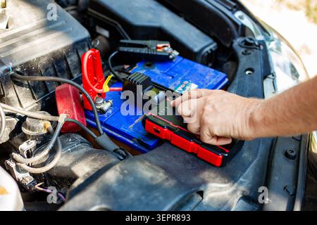 Using a compact jump starter device to start a car with a flat battery. modern automotive technology, emergency roadside help. Stock Photo