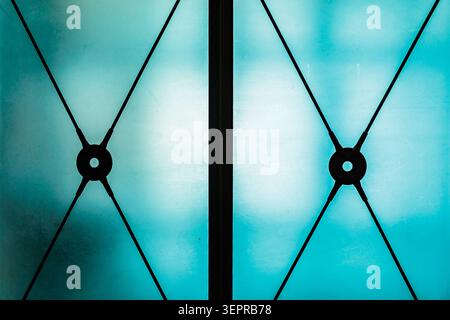 Blue-tinted glass skylight framed by dark metal grid and diagonal cables, creating a minimalist geometric pattern and cool, serene atmosphere in conte Stock Photo