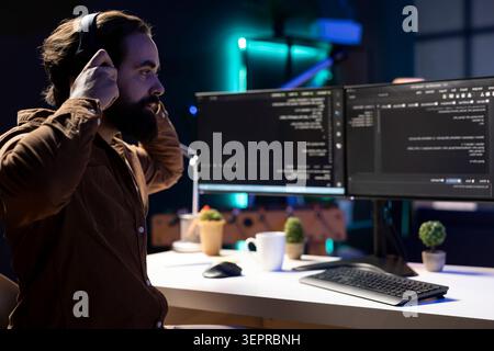 Programmer enjoying podcasts and futureproofing company network from downtimes and unexpected system failures; iT expert putting headphones on to listen audiobooks while increasing data security. Stock Photo