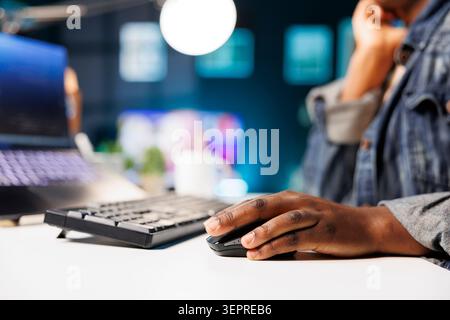 Hand of black person on a digital mouse, browsing coding information for a database; african american individual searching for information on online programming. Stock Photo