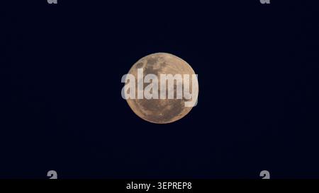 Detailed view of a full moon illuminated against a dark night sky. Astronomical image showing lunar surface features and natural satellite of Earth. Stock Photo