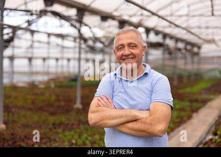 Old man worker posing joyfully in greenhouse Stock Photo