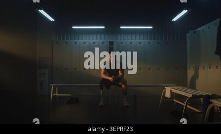Young Man with Prosthetic Leg Sits on Bench in Dimly Lit Locker Room, Focusing Mind and Building Motivation Before Standing Up to Start Workout Session. Mental Grit and Determination. Portrait. Stock Photo