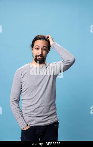 Middle eastern uncertain person feeling unsure and confused against blue background, contemplating and feeling curious in studio while young adult acting thoughtful and reflective, decision making. Stock Photo