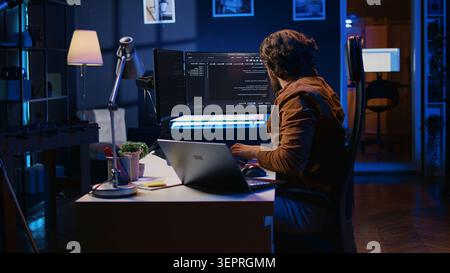 Software programmer putting headphones on while developing code, making time pass faster during remote job shift. IT professional doing multitasking in apartment office while listening music. Stock Photo