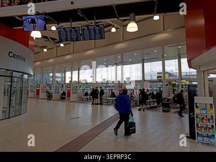 Early evening activity at Warrington Interchange, with passengers, seating, a bicycle and a yellow electric bus at Stand D. Stock Photo