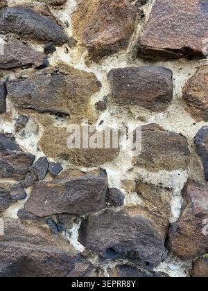 Weathered stone wall with irregular natural stones and light mortar, showing outdoor texture, colour variation and detailed surface pattern. Stock Photo