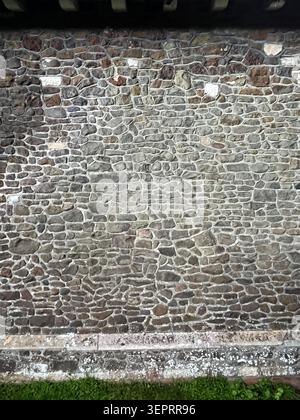 Weathered stone wall with irregular shaped stones and natural surface texture, showing colour variation and detail in an outdoor setting. Stock Photo