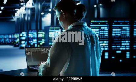 Experienced engineer running programming code on laptop, troubleshooting and updating data center equipment designed to accommodate server clusters, networking systems and storage arrays. Stock Photo