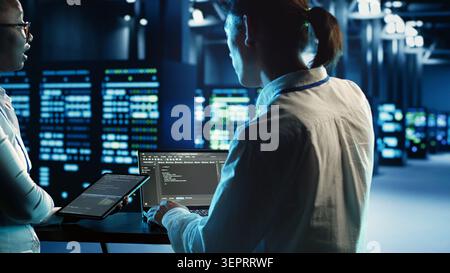 Engineering coworkers programming scripts on tablet and laptop, updating data center equipment designed to accommodate blade servers, networking devices and storage arrays Stock Photo