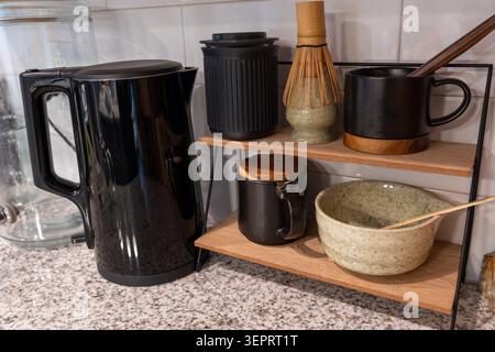 Kitchen counter with black kettle and wooden tea shelf holding matcha whisk, bowls, cups and canister. Minimal Japanese tea station concept Stock Photo