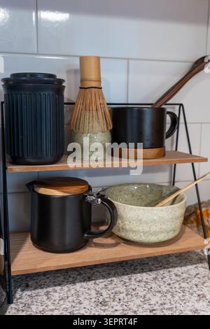 Vertical photo of tea ceremony essentials including a bamboo matcha whisk (chasen) on a ceramic holder, a black mug with wooden coaster, a black pitch Stock Photo
