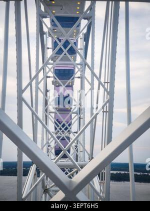 View from inside a Ferris wheel, showing colorful enclosed cabins framed by white steel beams against a bright sky. An abstract amusement park perspec Stock Photo