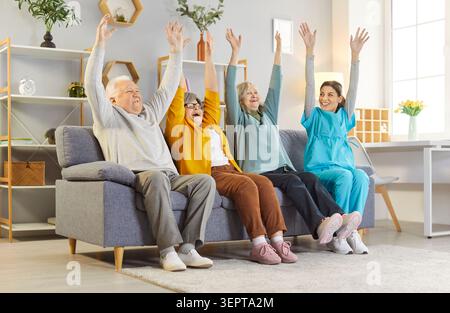 Senior people sitting on sofa with nurse and doing sport exercises in retirement home. Stock Photo