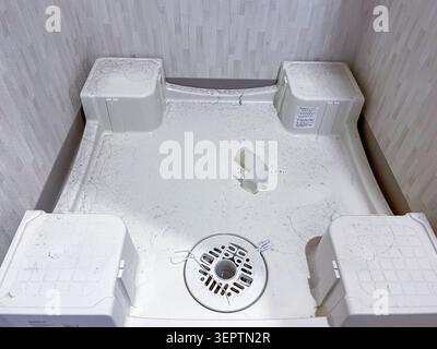 An overhead view of an empty plastic washing machine tray with a central drain and water supply connector in a Japanese apartment laundry space during hikkoshi (move-in preparation). Common in Japanese rental properties before appliance installation. Stock Photo