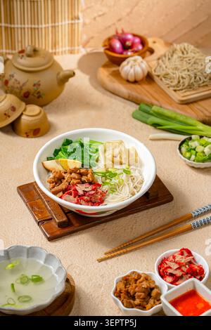 A delicious bowl of Asian rice vermicelli served with roasted char siu pork, seasoned chicken, wonton dumpling, bok choy, boiled egg, scallions, and l Stock Photo