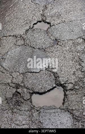 Cracked asphalt surface showing road damage and potholes with puddles Stock Photo