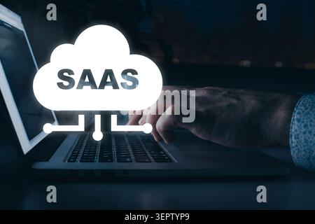 User typing on laptop with Saas concept in a dark office setting at night time Stock Photo