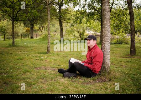 Man enjoying quiet time reading a book under a tree in a park Stock Photo