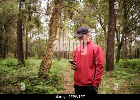 Man in red jacket checking smartphone on a woodland trail Stock Photo