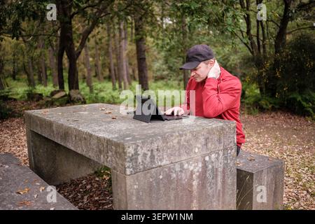 Man using a laptop at a stone table in the forest experiencing neck pain Stock Photo