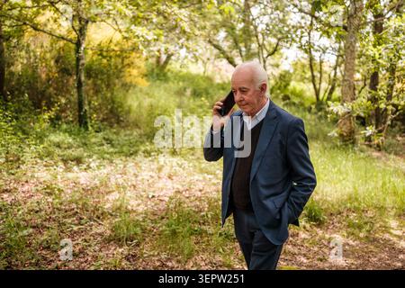 Mature man in suit making a business call walking through a green forest Stock Photo