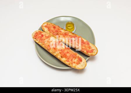 On a black slate board are arranged three slices of ciabatta bread, each spread with ripe fresh tomato, sprinkled with dried oregano, and accompanied Stock Photo