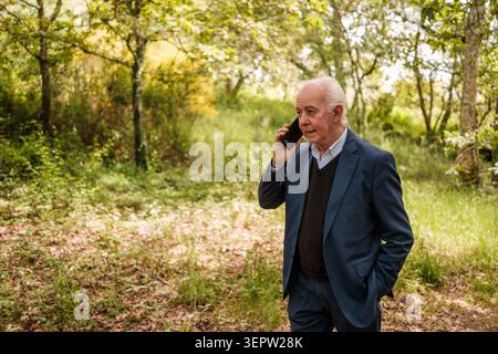 Senior businessman walking through a forest while having a phone conversation Stock Photo