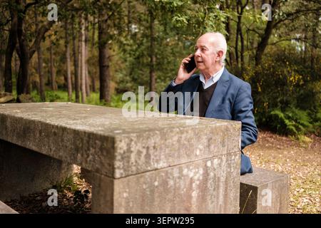 Senior man using a smartphone for communication outdoors sitting at a stone table Stock Photo