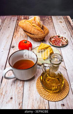 Glass olive oil cruet and white enamel pitcher beside bread basket, ham, tortilla chunks Stock Photo