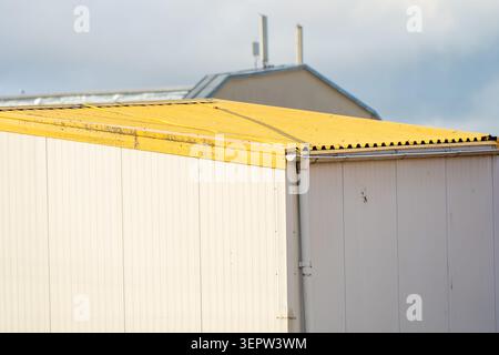 An exterior view of an industrial warehouse container facility with white sandwich panels and a weathered yellow metal roof structure Stock Photo