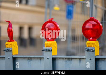 Three round red warning lights mounted on yellow bases attached to a steel safety barrier at an urban roadworks construction site Stock Photo
