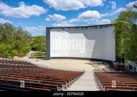 At Boskovice, Czechia, a summer cinema hosts outdoor movie screenings. The large screen stands ready for films, surrounded by rows of empty seats and green trees under a blue sky. Stock Photo