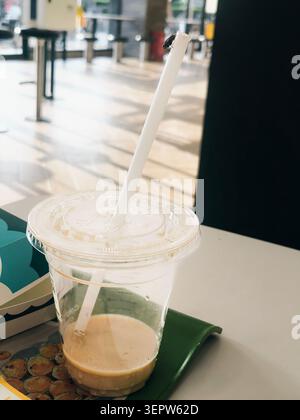 Iced coffee in clear plastic cup with straw on green tray inside modern café Stock Photo