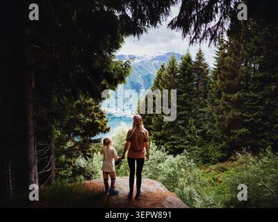 Family mother and daughter hiking in the woods explore Norway together, parent and child sightseeing fjord view above Odda town outdoor people on acti Stock Photo