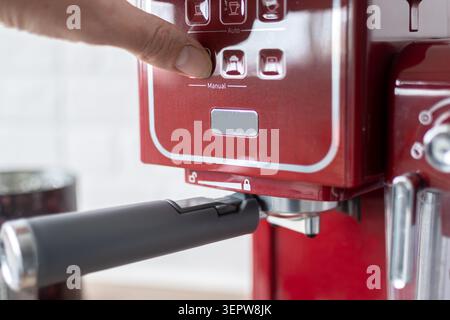 Close-up of a hand operating a red espresso coffee machine by pressing the brew button. Home coffee preparation concept featuring barista-style espres Stock Photo