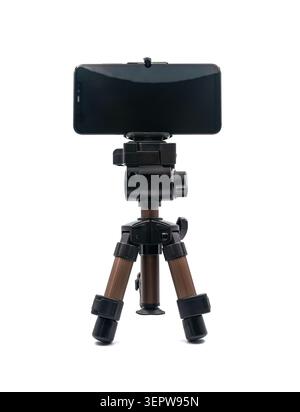 A black smartphone, mounted horizontally on a small compact tripod, stands against a white background. Stock Photo