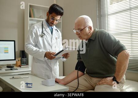 Senior Man Visiting Doctor during Blood Pressure Check in Clinic Stock Photo