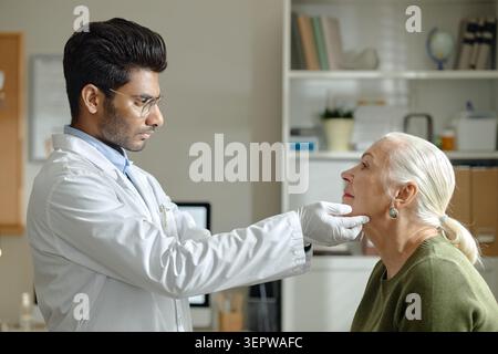 Indian Male Doctor Examining Senior Woman Neck in Clinic Visit Stock Photo