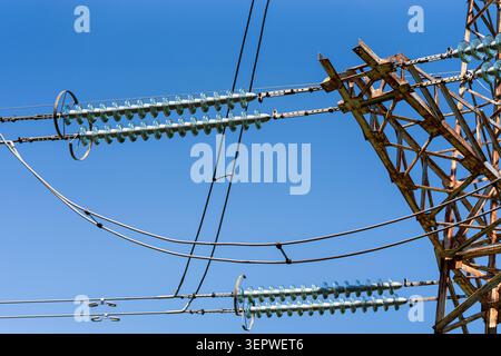 Close up of high voltage electricity pylon with glass cap insulators and power transmission cables against clear blue sky, electrical grid infrastruct Stock Photo
