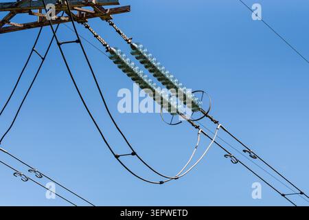 Close up of high voltage electricity pylon with glass cap insulators and power transmission cables against clear blue sky, electrical grid infrastruct Stock Photo