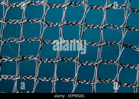 Detailed close up of a twisted metallic mesh with repeating square openings, showing a textured wire pattern against a solid blue background Stock Photo