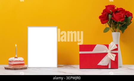 Birthday mockup with blank frame lit candle cake and gift box on yellow background Stock Photo