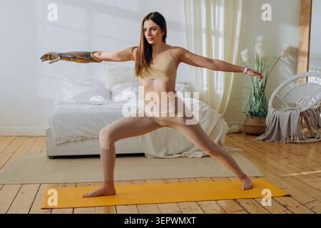 Woman with an advanced prosthetic arm confidently practicing a yoga pose on a mat, demonstrating empowerment, physical well being, and inclusion in an accessible fitness routine Stock Photo