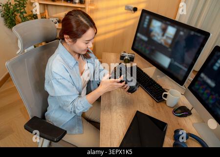 A professional female freelance photographer sits at her desk in a home office, editing digital photographs on a computer screen. Stock Photo