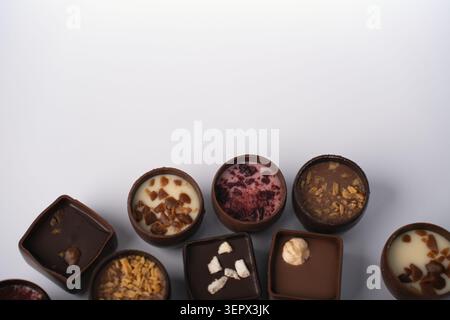 assorted artisanal chocolate bonbons and truffles arranged in a neat row on a clean white background, highlighting glossy milk and dark shells, creamy Stock Photo